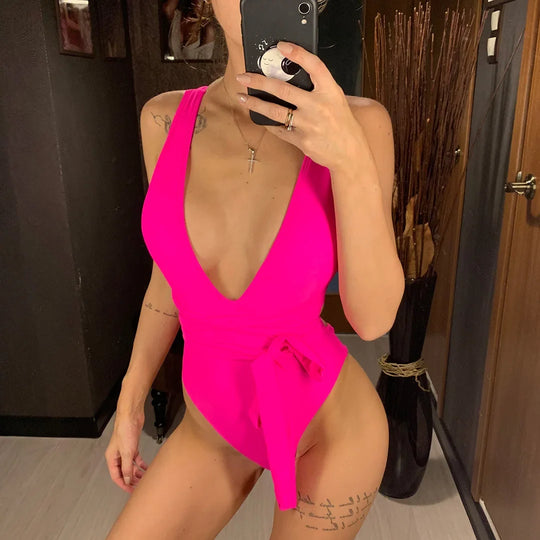 Maillot de bain une pièce triangle croisé rose fuchsia porté de face en selfie, décolleté plongeant et lien noué à la taille