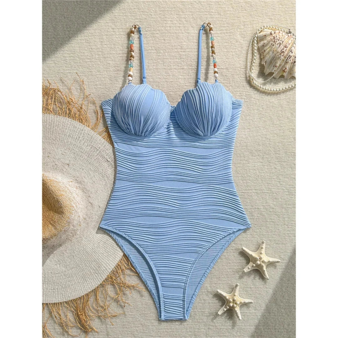 Maillot de bain une pièce à armatures bleu posé à plat sur le sable avec un chapeau de paille et des étoiles de mer