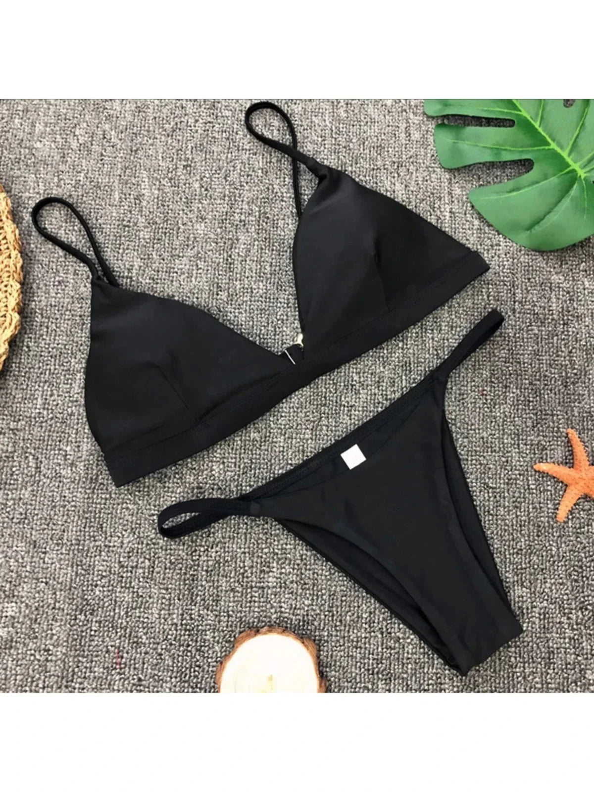 Bikini brésilien rembourré à taille basse noir posé à plat sur tapis gris, petite étiquette blanche sur le bas