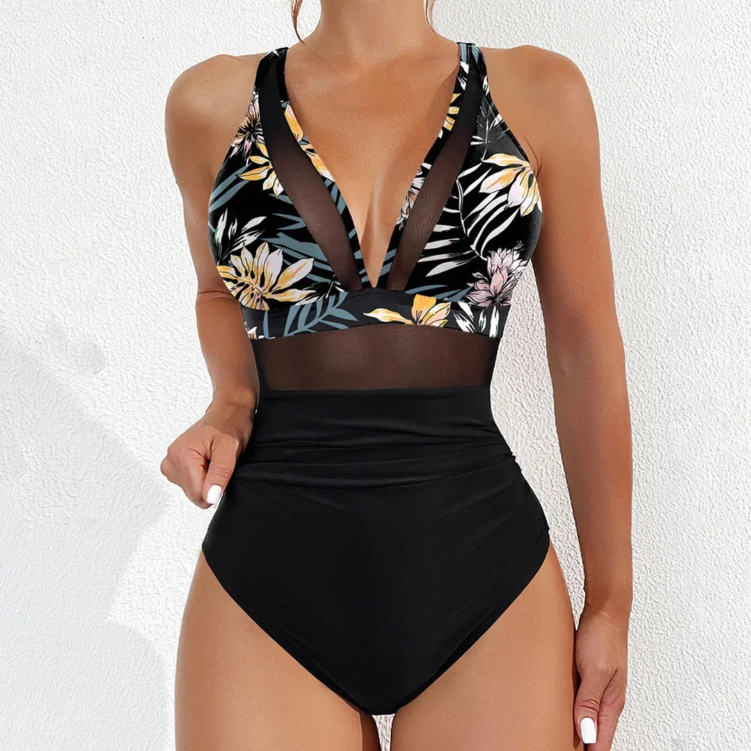 Maillot de bain une pièce en mesh imprimé feuilles porté de face par une femme, haut à fleurs et feuilles sur fond noir et bas noir uni