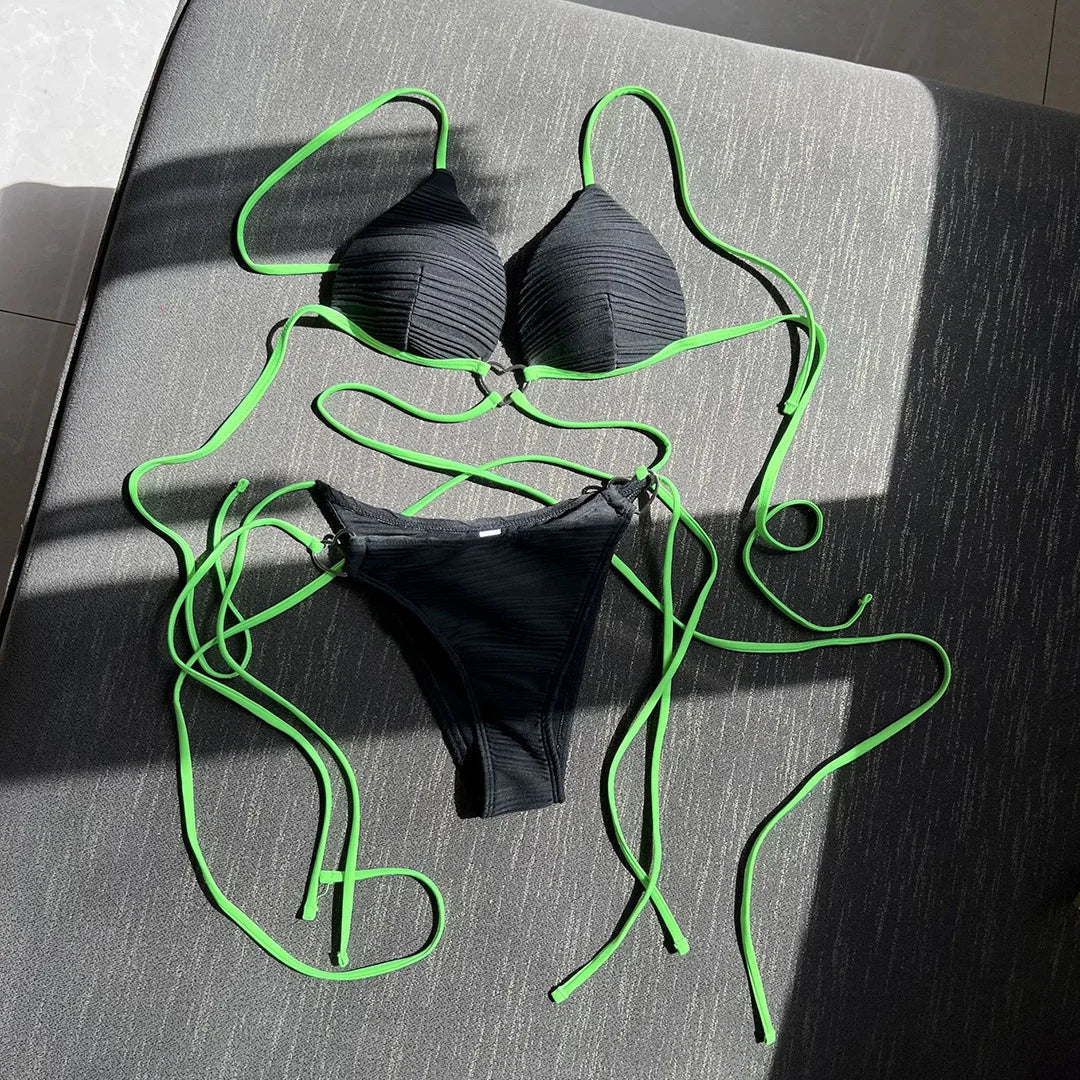 Bikini col halter croisé à effet froissé noir posé à plat, longs lacets vert fluo déployés et slip noir