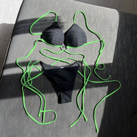 Bikini col halter croisé à effet froissé noir posé à plat, longs lacets vert fluo déployés et slip noir