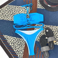 Bikini tour de cou à lacets croisés sans armatures bleu posé à plat sur un foulard à motifs, avec sandales grises
