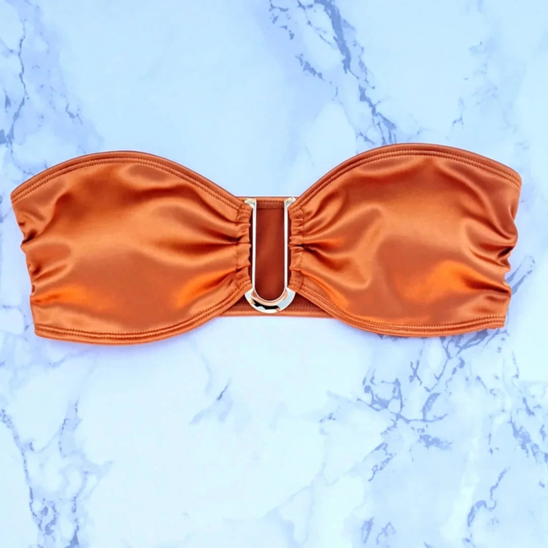 Gros plan sur le haut orange du bikini bandeau, anneau métallique en D au centre et plis du bandeau