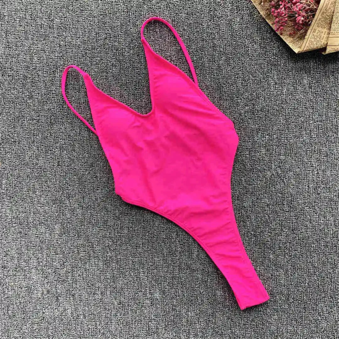 Maillot une pièce rose fuchsia à plat sur un tapis gris, bretelles fines et coupe string haute