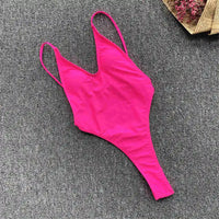 Maillot une pièce rose fuchsia à plat sur un tapis gris, bretelles fines et coupe string haute