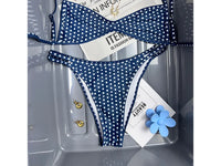 Bikini bralette taille basse bleu marine à pois blancs et bas échancré, posé à plat avec des accessoires