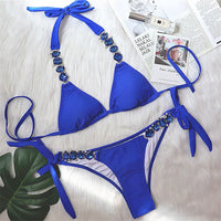 Bikini brésilien à strass effet diamant brillant bleu roi à plat sur une fourrure blanche, feuille verte et magazine