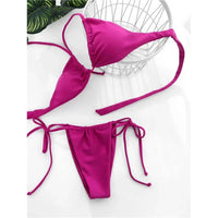 Bikini string mini tour de cou taille basse rouge et violet fuchsia posé à plat devant une corbeille, lacets longs étalés
