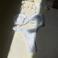 Bikini brésilien texturé froissé blanc posé à plat sur un tapis, ombre du soleil et coquillages autour