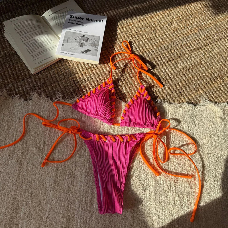 Bikini tour de cou rose vif à liens orange posé à plat sur une natte, livre ouvert à côté
