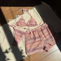 Ensemble rayé rose pêche posé à plat sur un tapis en tissu, haut à lanières, short taille élastique et bas ficelé