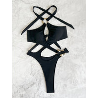 Maillot une pièce col halter noir posé à plat sur du marbre blanc, bretelles croisées au cou et anneaux dorés