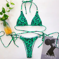 Bikini string croisé sans armatures taille basse imprimé léopard vert posé à plat sur un magazine, bretelles fines et anneau