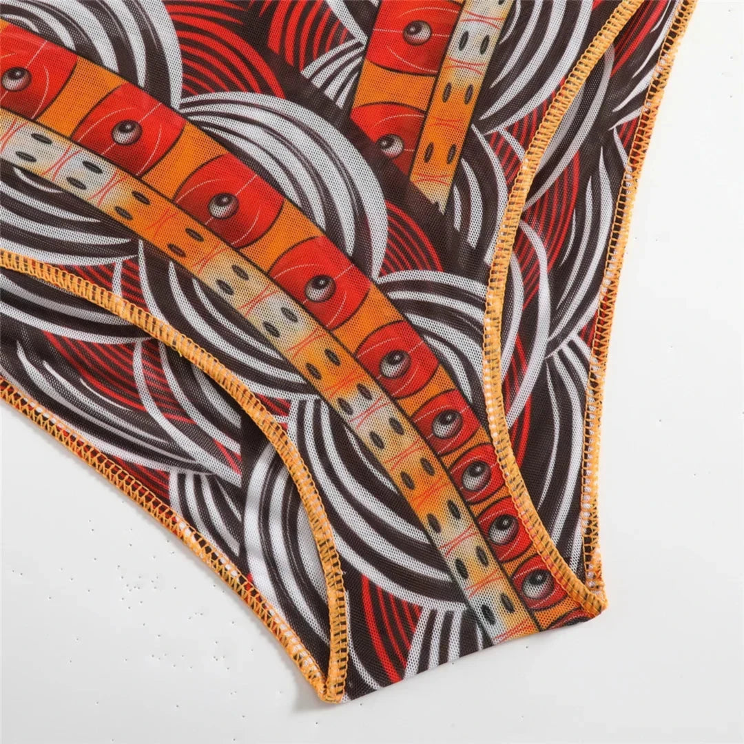 Gros plan sur le bas du maillot une pièce imprimé ethnique, liseré orange fin et motifs en vagues grises et noires