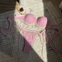 Bikini côtelé à armatures bords festonnés rose étalé sur une nappe en dentelle, liens noués sur la culotte