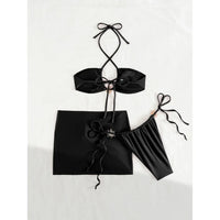 Maillot de bain trois pièces jupe halter à brides noir photographié à plat sans accessoires, nœud central sur la jupe et bas latéral