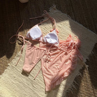 Maillot rose pêche à plat vu de l'intérieur, doublure blanche visible sur le haut à liens et pareo volanté posé à côté