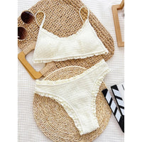 Bikini à volants beige effet froissé posé à plat sur un tapis en osier, haut à bretelles et culotte froncée