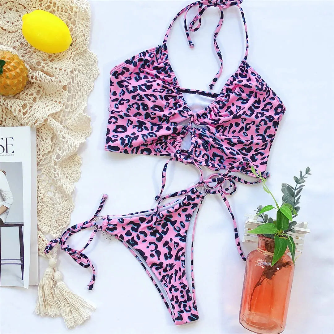 Bikini deux pièces tour de cou léopard rose posé à plat sur fond blanc, avec un citron et un magazine