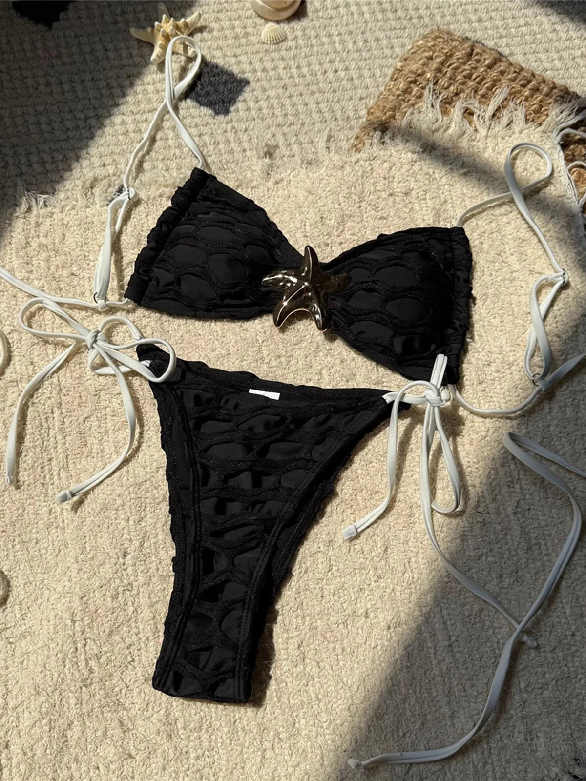 Bikini échancré à lanières et étoile métal noir posé à plat sur un tapis, étoile au centre et bas à lanières latérales