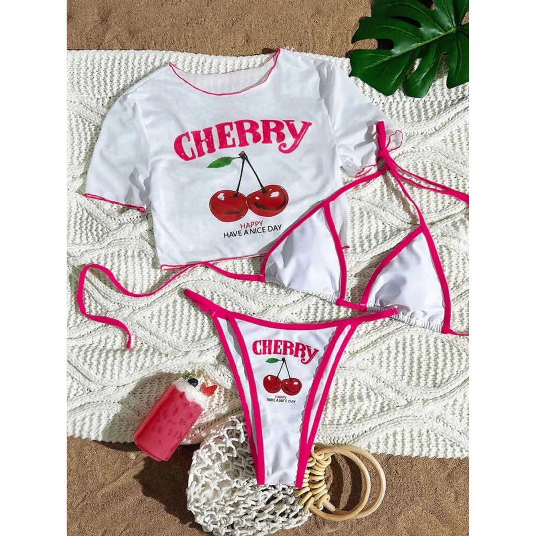 Maillot trois pièces cerises blanc bordé rose fuchsia, crop top et bikini posés à plat sur un tapis en tricot
