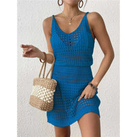Tunique de plage en crochet ajourée bleue portée de face, sac en paille tenu à la main, sur un mur blanc