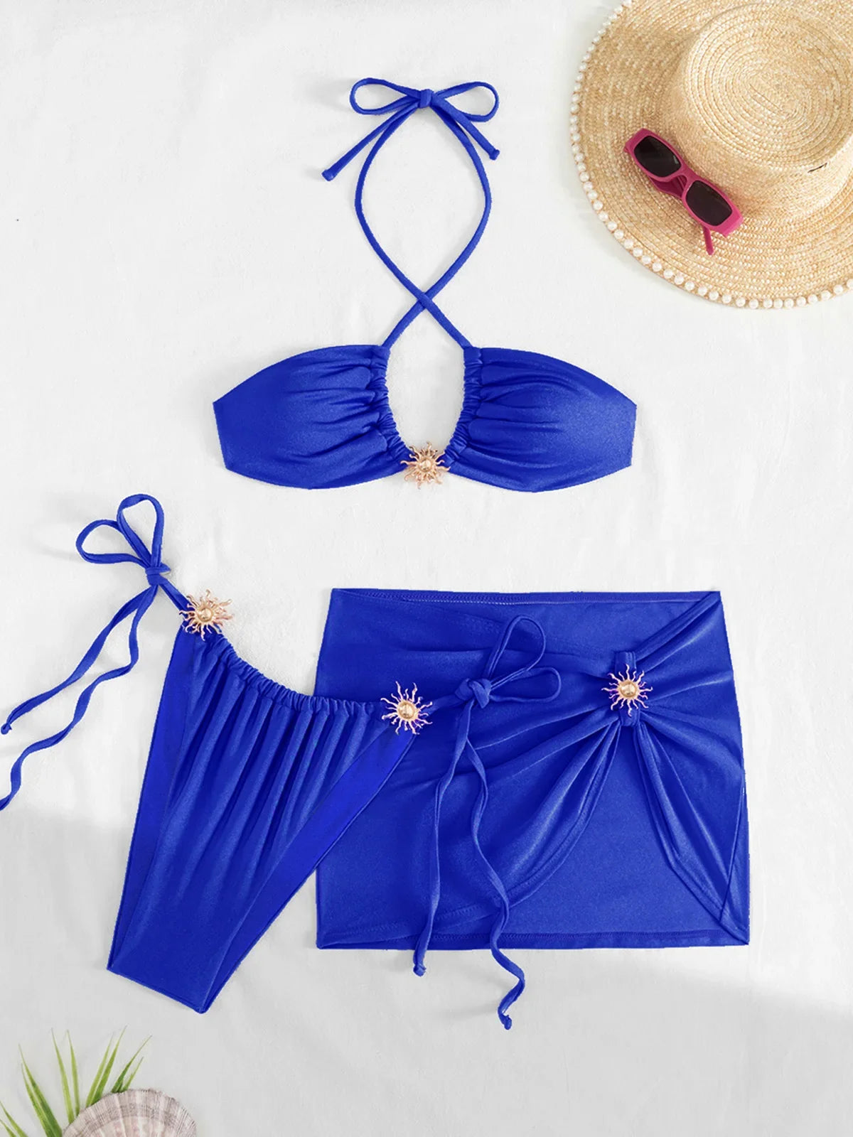 Maillot de bain trois pièces jupe halter à brides bleu posé à plat sur fond blanc, avec bas à brides et jupe nouée sur le devant