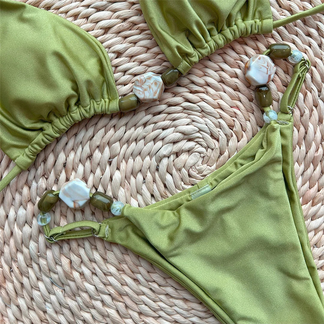 Gros plan sur les bretelles et le slip du bikini brillant tour de cou vert, perles nacrées et anneaux sur les côtés