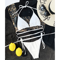 Bikini brésilien blanc étalé à plat sur une chemise noire à motif léopard, avec un chapeau de paille et des citrons jaunes