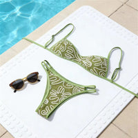 Bikini brésilien vert à motifs blancs posé à plat sur un tapis près d'une piscine, lunettes de soleil à côté