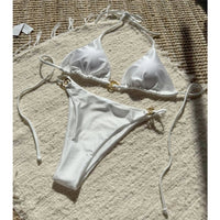 Bikini tour de cou à anneau métallique blanc posé à plat sur un tapis en fibres, anneaux dorés au haut et au bas
