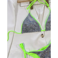 Gros plan sur le haut argenté brillant à liseré vert fluo et les lacets fins du bas, posé sur un tissu blanc