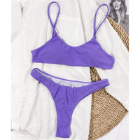 Bikini string brassière violet posé à plat sur une chemise blanche, à côté d'un chapeau en paille