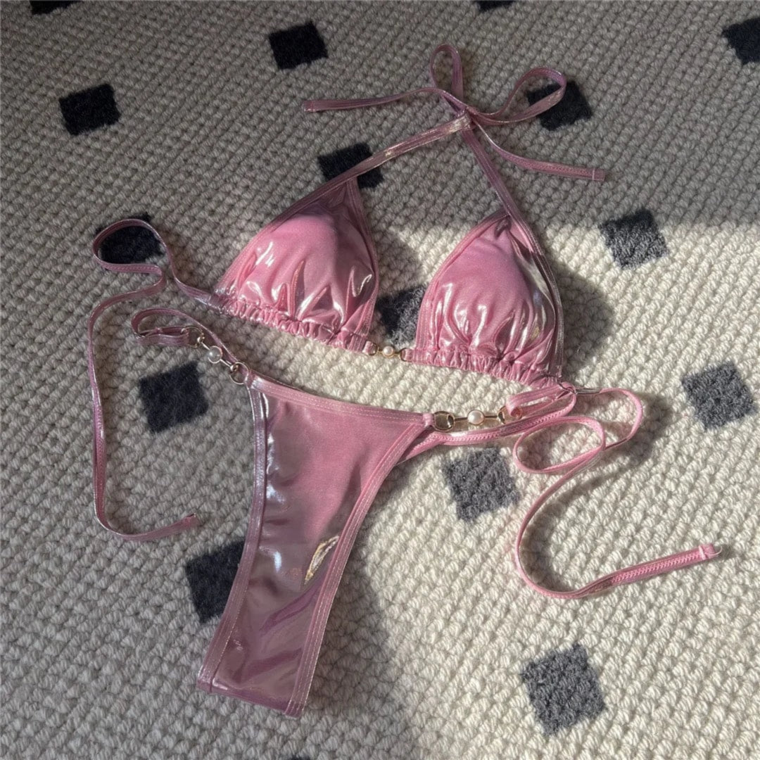 Bikini tour de cou et bas string en similicuir rose vif posé à plat sur un tapis, liens latéraux et reflets brillants