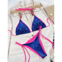 Bikini brésilien tour de cou sans armatures bleu à reflets posé à plat sur une veste blanche, sous un cintre