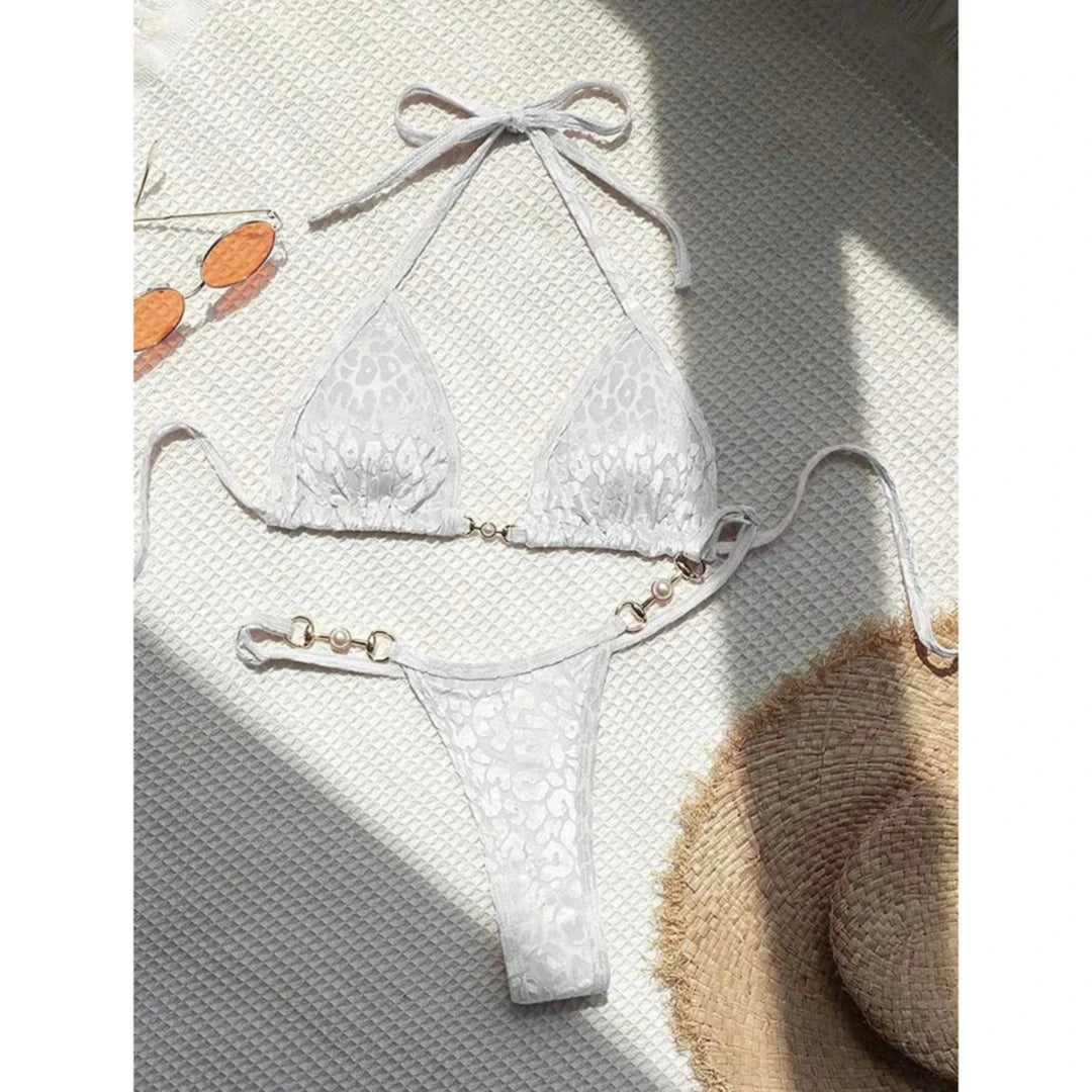 Bikini string triangle sans armatures imprimé léopard blanc posé à plat sur fond gris, bretelles étalées et ombre