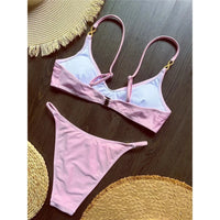 Bikini triangle rose vu de dos posé à plat sur une table en bois, doublure blanche visible et bretelles croisées