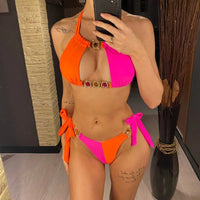 Bikini deux pièces à strass patchwork rose fuchsia et orange porté de face par une femme devant un miroir, anneaux dorés ornés de strass