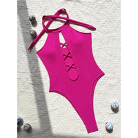 Maillot de bain une pièce col haut à lacets rose vif posé à plat sur un tissu blanc, coquillages et bretelles croisées