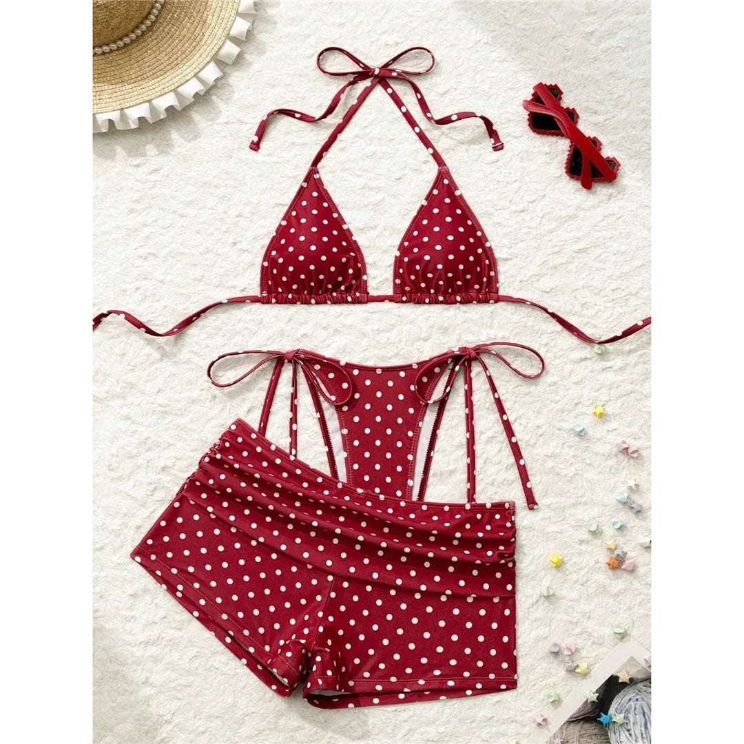 Maillot trois pièces à pois rouge posé à plat sur une surface blanche, avec lunettes et chapeau de paille