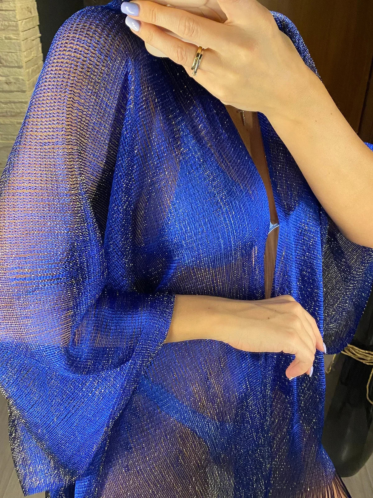 Gros plan sur la maille bleue brillante de la tunique de plage à franges, fils scintillants et manche ample