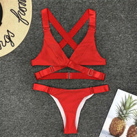 Bikini sans armatures croisé dans le dos rouge posé à plat sur un tapis gris, bretelles croisées et boucle centrale
