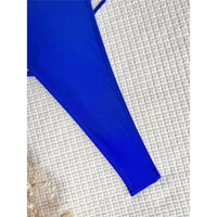 Gros plan sur le bord latéral échancré d'un maillot une pièce bleu roi posé sur un tissu blanc
