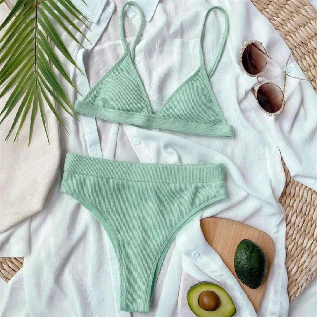 Bikini taille haute côtelé sans armatures vert menthe posé à plat sur une chemise blanche, avec un avocat