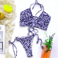 Bikini deux pièces léopard violet à lacets posé à plat sur une serviette en crochet, avec un citron et un verre