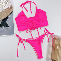 Bikini deux pièces tour de cou à lacets rose fuchsia posé à plat, avec un magazine et un vase en verre