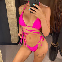 Bikini brésilien rose fuchsia porté de face par une femme en pied, mains le long du corps, lacets noués sur les hanches