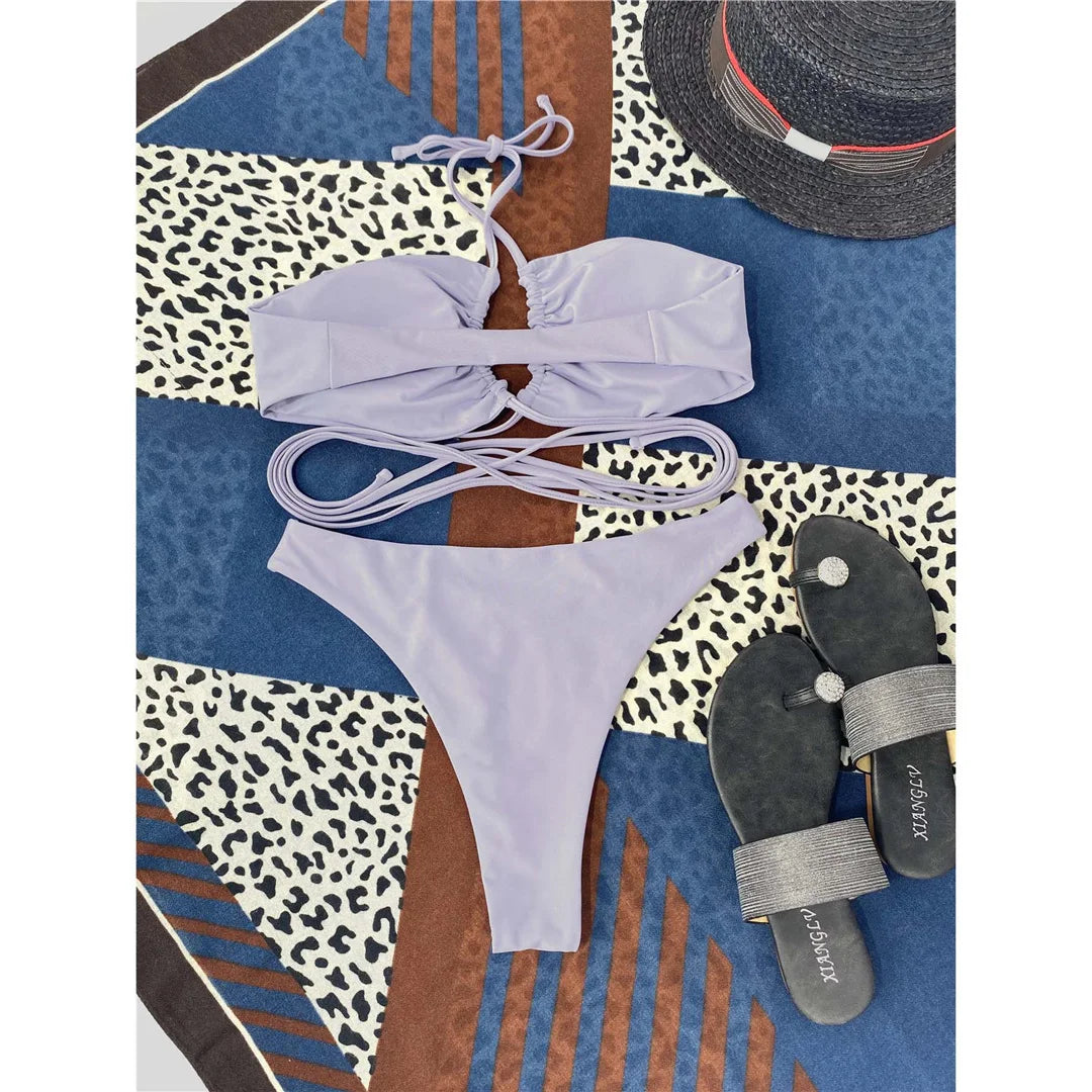 Bikini tour de cou à lacets croisés sans armatures gris posé à plat sur un foulard, avec chapeau et sandales grises