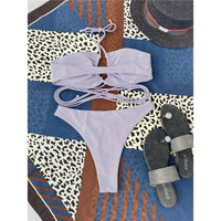 Bikini tour de cou à lacets croisés sans armatures gris posé à plat sur un foulard, avec chapeau et sandales grises